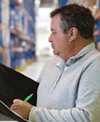 TCC Transfer Student Joe Holder stands in a warehouse writing notes in a folder.