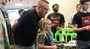 Cody Fimple looks on as Masyn Fimple uses a remote control to compete in a combat robotics match