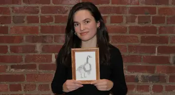 Sophia Freudenberger holds up her drawing that won the holiday card contest. It is a small, pencil drawing of a Canada goos with a wreath around its neck.