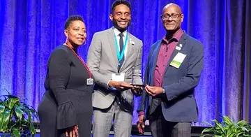 A woman presents the NOSS Award to Douglas Allen and Dewayne Dickens.
