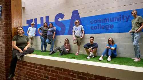 Students from Tulsa Community College stand together in front of a mural in the Fireplace lounge at TCC Metro Campus.