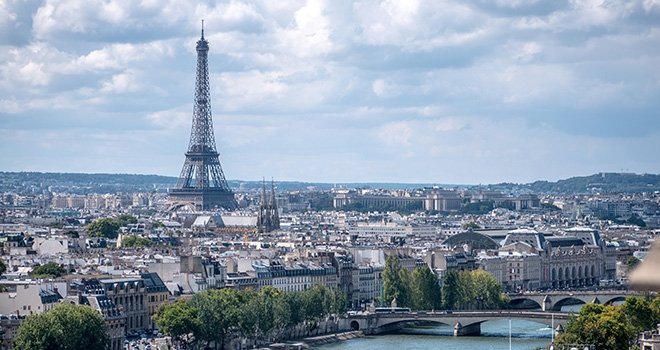 Wide cityscape view of Paris, France with the Eiffel tower In the distance and the Seine rive in the foreground.