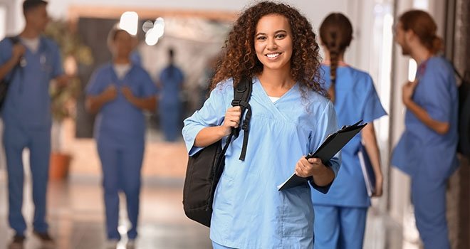 A woman in nurse scrubs holding a backpack and binder.
