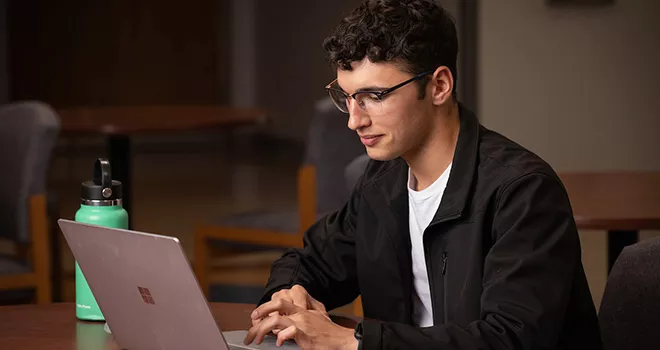 TCC student works a laptop ind a dark room.