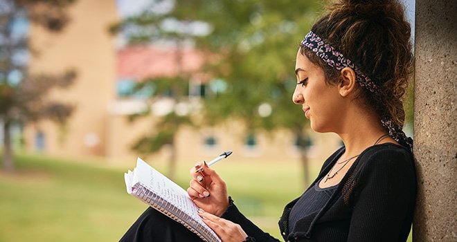 TCC student sits on campus and writes in her notebook.