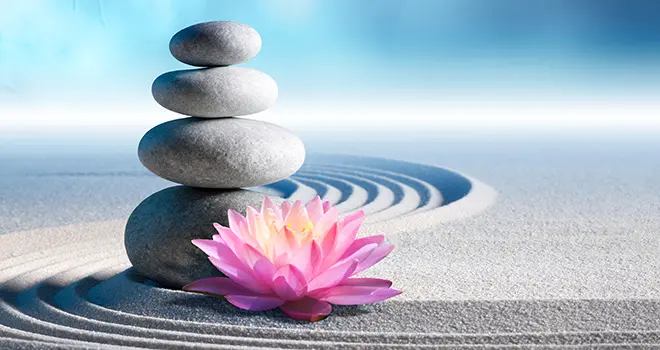 Stones stacked up with a lotus blossom in a sand zen garden