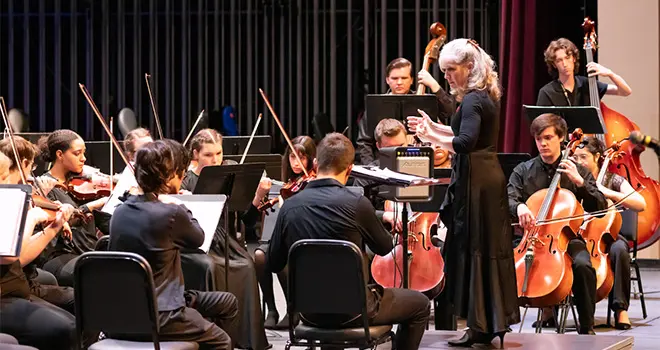 Orchestra students watch their conductor as they rehearse.