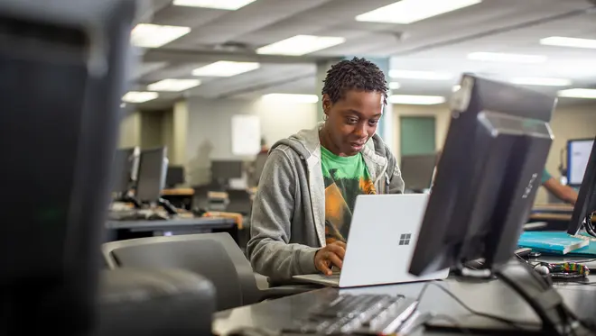 A student sits at a desk and types on a laptop computer