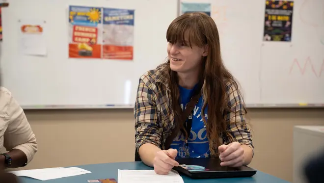 Natasha sits a table in the Language Lab. She is conversing with other people out of frame.