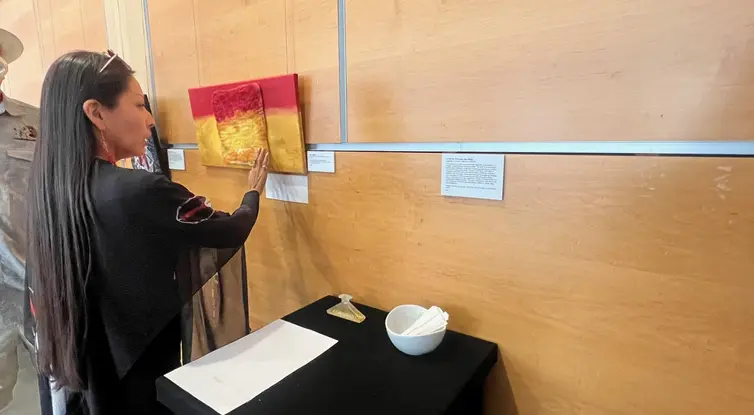 Photo of woman touching a piece of flat art hanging on a wall with a scent exhibit in the foreground.