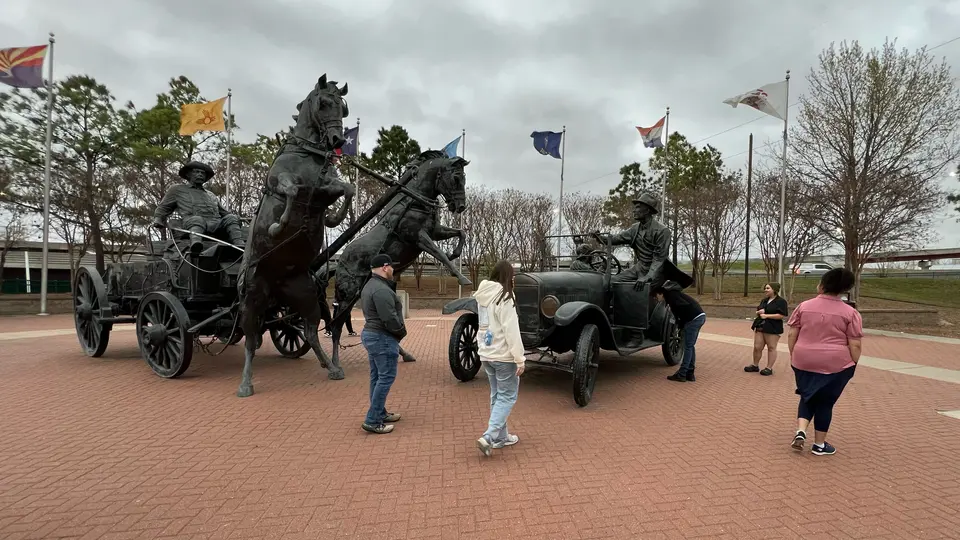 Three people look at ststaues at Cyrus Avery Centennial Plaza. The statues are of a man in a buggy being pulled by two horses and a man in a car.