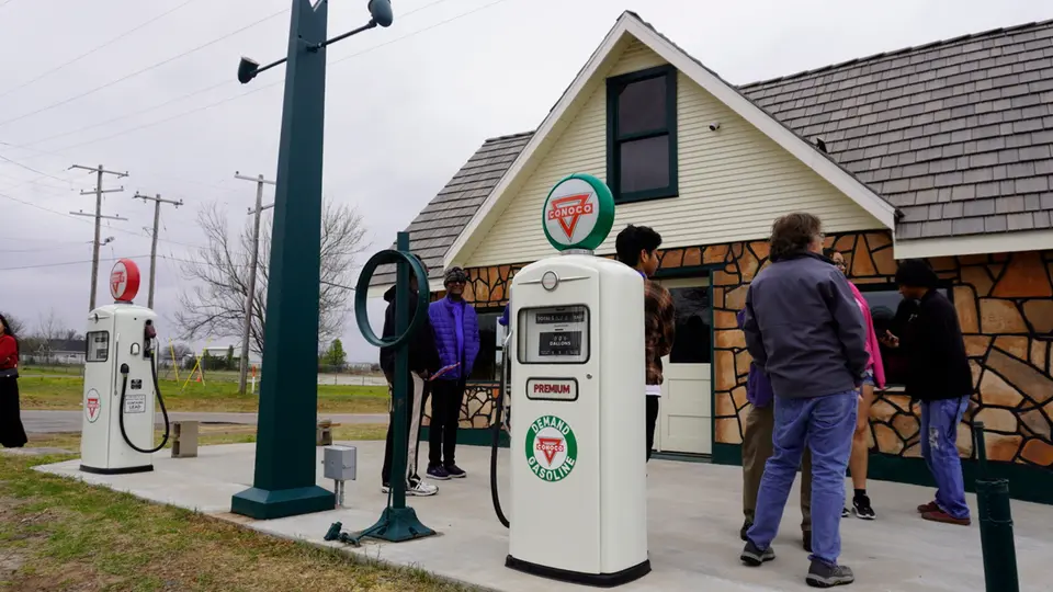 A few people look at the Threatt Filling Station. They are standing near two gas pumps.