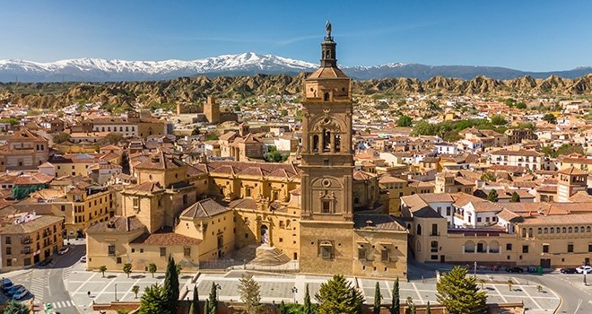 Aerial view of Guadix old town, province of Granada, Andalusia, Spain. Historic Cathedral building, Alcazaba de Guadix fortress and snow capped Sierra Nevada mountain range at background