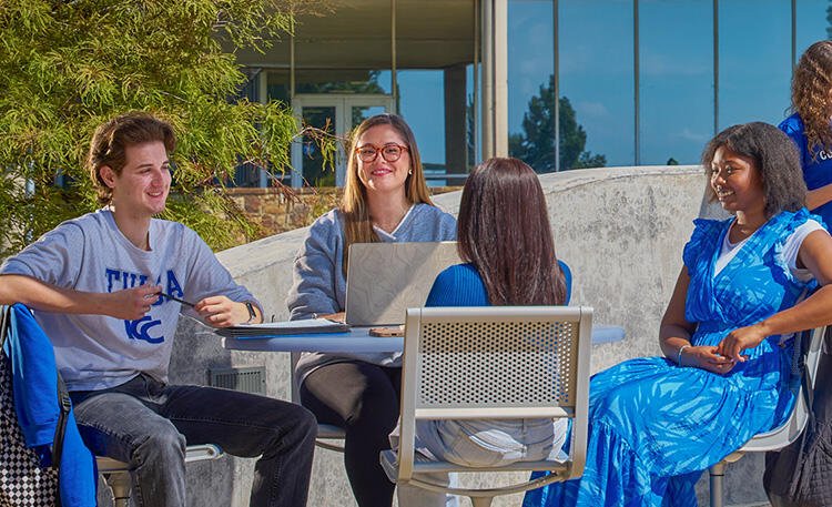 Four students gather at a table on the pond‑side patio at TCC’s Southeast Campus.