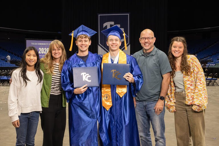 Six members of the Campbell family poses together for a photo with Hudson and Everett in the middle in blue graduation regalia and holding their TCC degrees